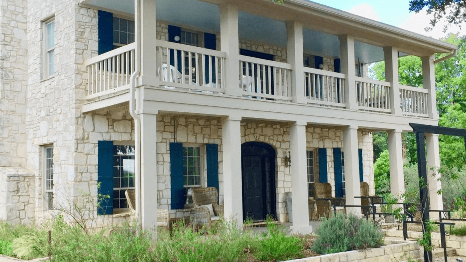 A charming two-story stone house with a large porch and blue shutters.