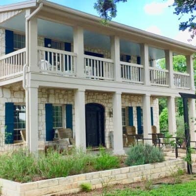 Two-story house with stone walls, blue shutters, and a spacious front porch.