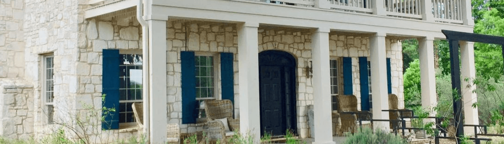 Exterior of a house featuring stone walls, blue shutters, and a welcoming porch.